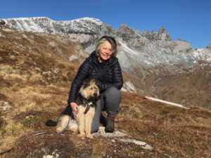 Hunde Wandern: eine Frau und ihr Hund bei einer Wanderpause, beide sitzen, hinten sieht man Berge