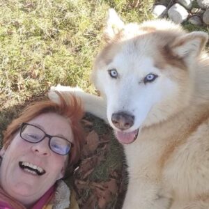 Eine Frau und ihr Hund liegen im Grad, beide schauen in die Kamera